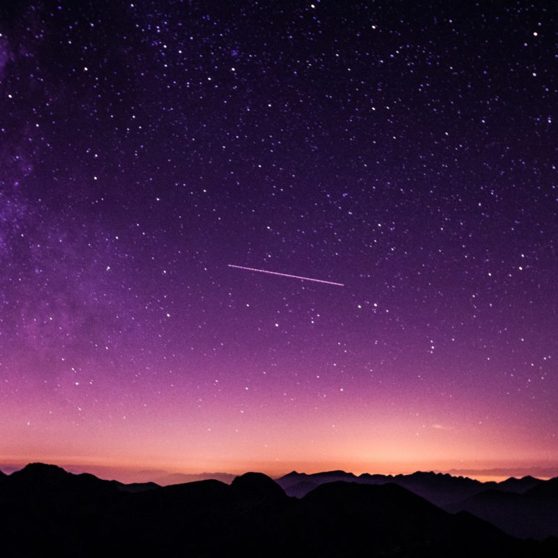 Shooting star in night sky above mountains
